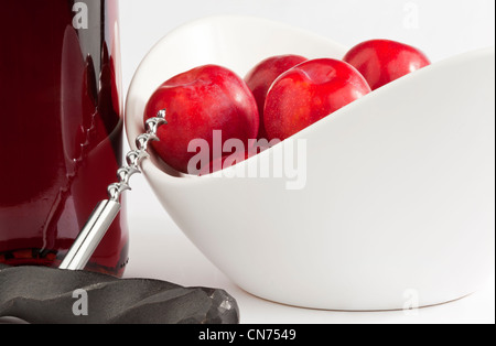 Prugne rosse in una vaschetta di colore bianco con una bottiglia di rosso/rosa del vino e un cavatappi Foto Stock