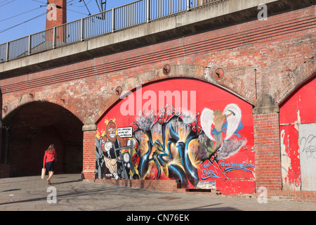 Scena urbana con la donna a piedi passato graffiti arte pittura sotto il vecchio ponte ferroviario archi. Leeds West Yorkshire England Regno Unito. Foto Stock