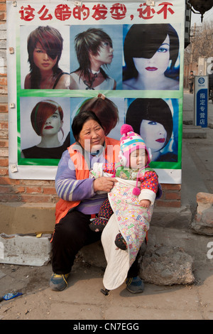 Pechino, Qikeshu (sette alberi) Village. Nonna con il nipote di fronte un parrucchiere. Foto Stock