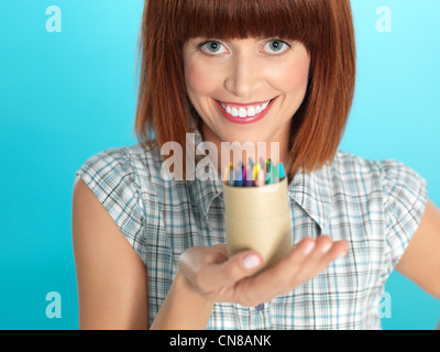 Bella giovane donna, tenendo abox di colori pastelli, sorridente, su sfondo blu Foto Stock