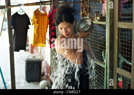 Una bella donna birmano lavaggi se stessa di fronte alla sua casa in una strada a Rangoon, Birmania Foto Stock