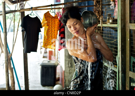 Una bella donna birmano lavaggi se stessa di fronte alla sua casa in una strada a Rangoon, Birmania Foto Stock