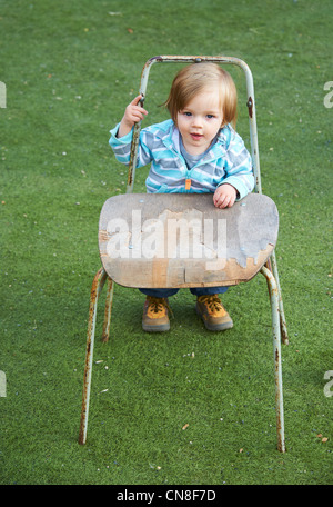 Baby girl bambino in piedi con la vecchia sedia in erba verde campo Foto Stock