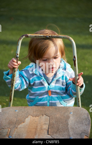 Baby girl bambino in piedi con la vecchia sedia in erba verde campo Foto Stock