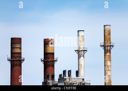 Quattro pile di fumo sulla cima di fabbriche o edifici industriali nella skyline. Foto Stock