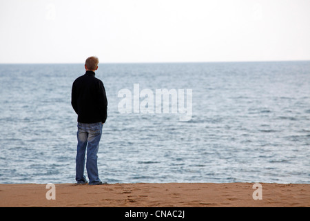 Un uomo in piedi su una spiaggia che guarda al mare in Sicilia, Italia Foto Stock