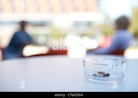 Skoking in luoghi pubblici di concetto - close-up di un posacenere su una terrazza di un caffè con persone (non fumatori) in background Foto Stock