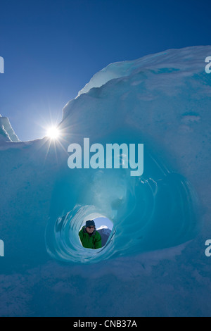 Composito: Persona guardando attraverso un piccolo tunnel erosi in un iceberg congelati in Mendenhall Lago, Juneau, Alaska, inverno Foto Stock