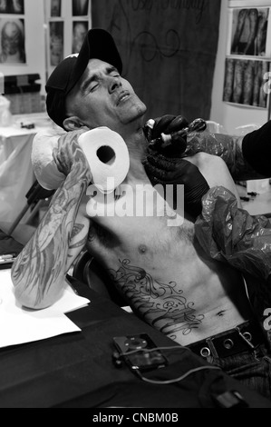 Un uomo indietreggia nel dolore mentre è tatuato al Edinburgh Tattoo Convention 2012 a Edimburgo, Scozia. Foto Stock