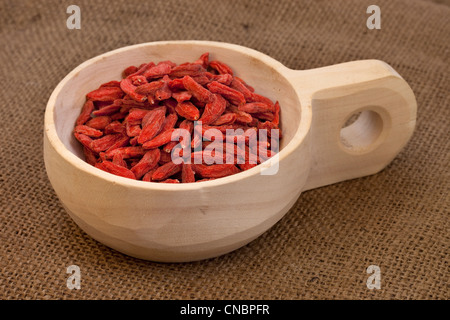 Essiccato Tibetan goji bacche (wolfberries) su un rustico in legno incompiuto scoop, sullo sfondo di tela Foto Stock