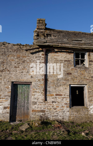 Una casa abbandonata e fabbricati agricoli, un rivestimento a superficie ruvida a porta peeling con macerie che circonda, man mano che si scende verso la rovina Foto Stock
