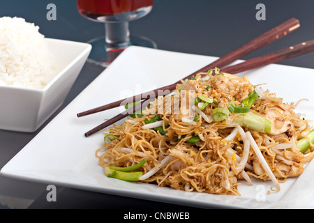 Un piatto tailandese di pollo e tagliatelle stir fry presentato su un quadrato bianco con piastra di bacchette di legno. Foto Stock