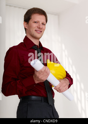 Metà adulto architetto con casco, tenendo blueprint e guardando fiduciosi in telecamera Foto Stock