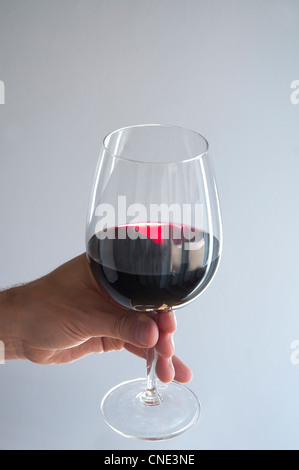 Mano d'uomo con in mano un bicchiere di vino rosso. Foto Stock