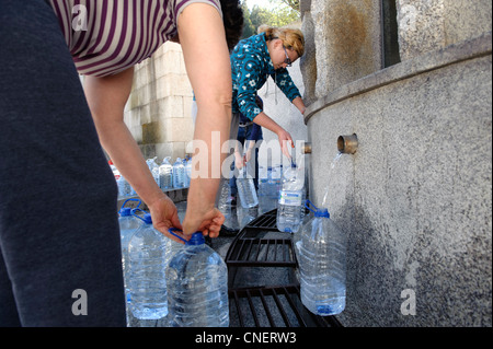 La gente di riempimento caraffe di acqua ad una fontana pubblica in Luso, Portogallo Foto Stock