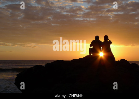 Felice coppia seduta sulla roccia a guardare molto romantica luminoso colorato tramonto sera spazio di copia Foto Stock