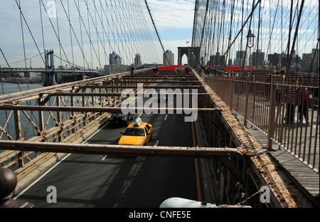 Blue sky view, verso Brooklyn, la gente sul passaggio pedonale sopra a traliccio metallico road-deck auto taxi gialli, Ponte di Brooklyn NY Foto Stock