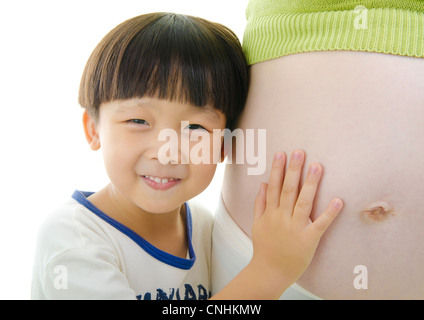 Piccolo ragazzo asiatico ascoltando la sua gravidanza madre ventre Foto Stock