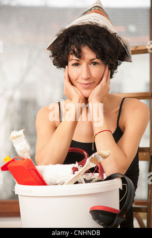 Una donna che indossa un cappello di carta appoggiata su una benna di materiali di consumo vernice Foto Stock