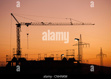 Una gru da cantiere e elettricità tralicci stagliano contro un Cielo di tramonto Foto Stock