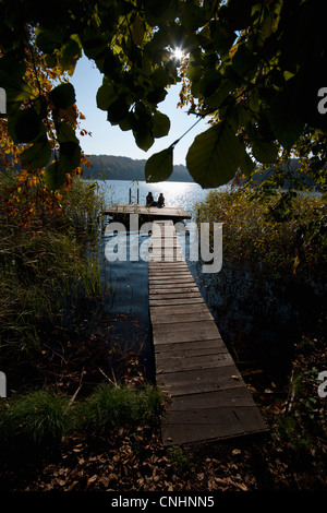 Due persone sedute al termine di un lungo pontile, stagliano Foto Stock