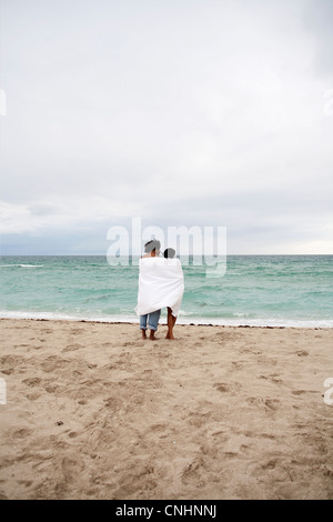 Una coppia giovane avvolto in un telo da spiaggia permanente sulla spiaggia Foto Stock