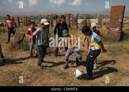 I bambini giocano a calcio tra khachkars nel famoso cimitero Noratus nella provincia di Gegharkunik, Armenia. Foto Stock