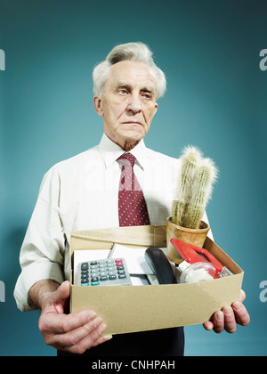 Un anziano uomo che porta una scatola di possedimenti dopo essere licenziato Foto Stock