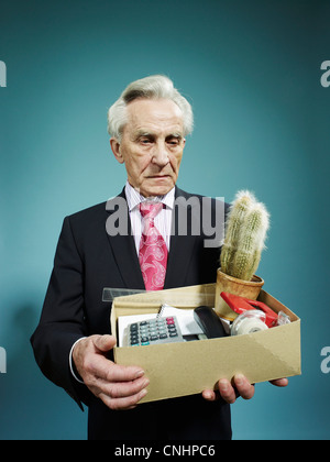 Un anziano uomo che porta una scatola di possedimenti dopo essere licenziato Foto Stock