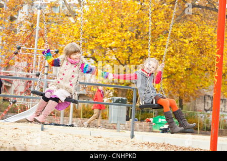 Due ragazze su altalene tenendo le mani Foto Stock