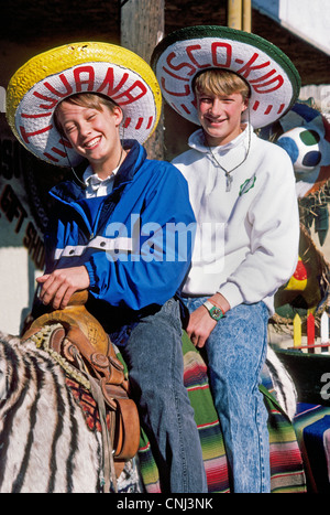 Due sorridente ragazzi americani montare un asino a strisce come una zebra di posa per foto in silly messicano cappelli sombrero durante la loro visita a Tijuana, Messico. Foto Stock