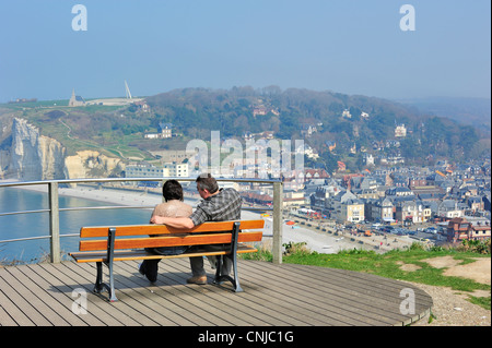 Giovane su banco guardando sopra la spiaggia e la città Etretat da Porte d'Aval, Côte d'Albâtre, Alta Normandia, Francia Foto Stock