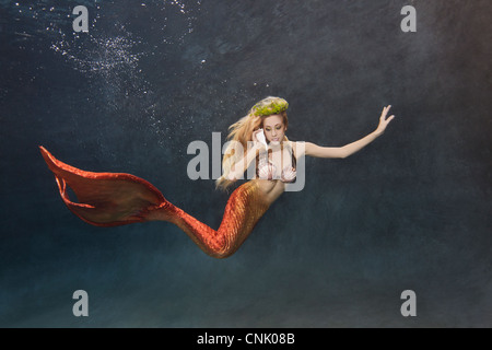 Giovani mermaid nuoto sott'acqua mentre si parla sul suo shellphone Foto Stock