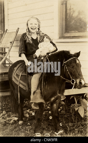 Ridere bambina con una bambola in sella a un pony Foto Stock