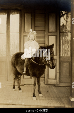 Bambina a cavallo di un pony sul portico Foto Stock