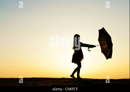 Ragazza giovane spinning con un ombrello al tramonto. Silhouette Foto Stock