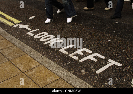 Regno Unito. Londra. Avvertenza sulla strada dell'obbligo di guardare a sinistra prima di attraversare la strada. Il West End. Foto Stock