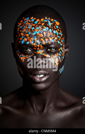 Nero africano giovane maschio modello indossando creative arancione e blu vernice tribali sul volto, fotografato in un ambiente di studio. Foto Stock