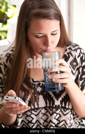 Casual giovane donna gode di un fresco drink mentre texting. Foto Stock