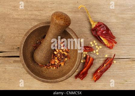 Secchi peperoncino rosso e semi con un pestello e mortaio sul vecchio legno rustico Foto Stock