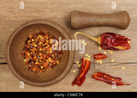 Il pestello e mortaio con secchi peperoncino rosso, fiocchi e semi su un vecchio weathered tagliere in legno Foto Stock