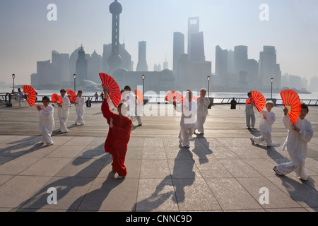 Persone che praticano il Taiji con ventole rosso sul Bund, Pudong skyline di distanza, Shanghai, Cina Foto Stock