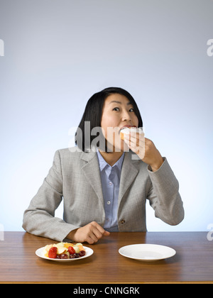 Imprenditrice ciambella di mangiare alla scrivania Foto Stock