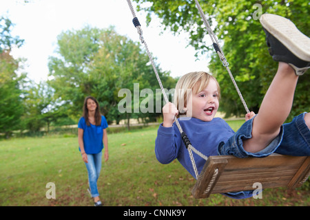 Ragazzo giocando su altalena in cortile Foto Stock