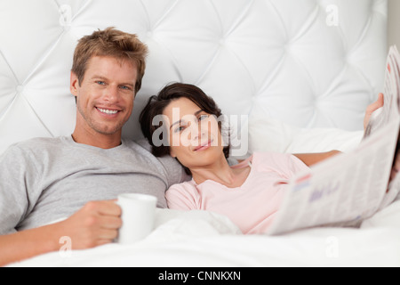 Sorridente giovane leggendo il giornale in bed Foto Stock