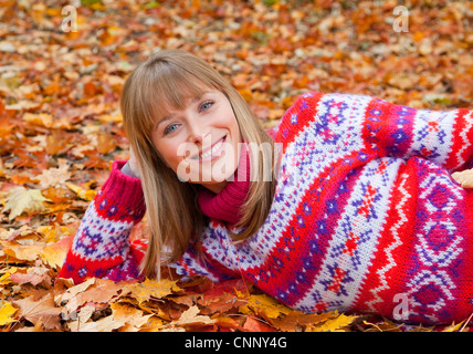 Donna sorridente posa in foglie di autunno Foto Stock