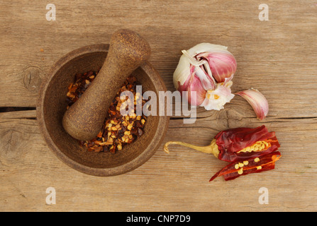 Fiocchi di peperoncino in un pestello e mortaio con aglio e tagliare il peperoncino su un vecchio weathered tagliere in legno Foto Stock