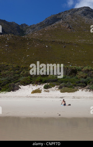 Un uomo seduto nella sabbia sulla spiaggia, a Kogel Bay, Western Cape, Sud Africa Foto Stock