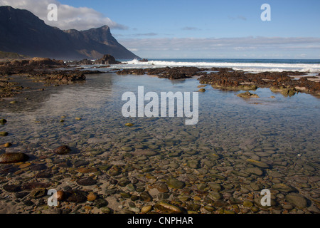 Kogel Bay Beach con rock in primo piano della montagna, a Kogel Bay, Sud Africa Foto Stock