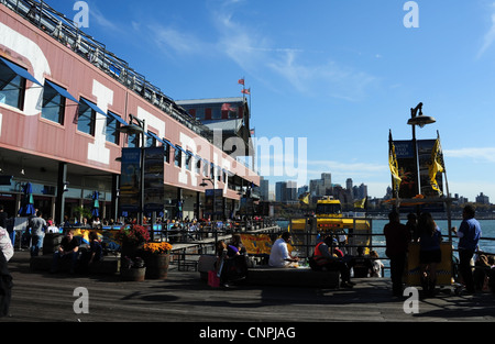 Blue sky view, verso East River taxi d'acqua, la gente seduta a piedi sotto il nome di Bianco Pier 17, South Street Seaport, New York Foto Stock